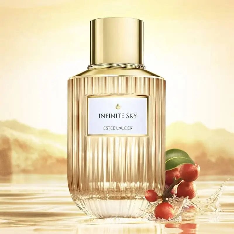 A creative and beautiful product photo of the Estée Lauder Infinite Sky perfume bottle, set against a glowing sunset and water, with red berries and a leaf in the foreground, suggesting its natural and warm notes.