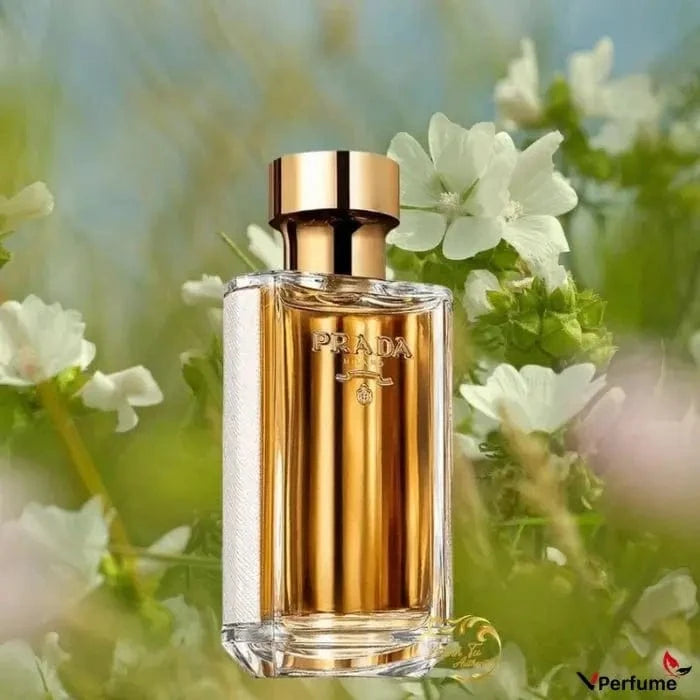 A stylized photo of the La Femme Prada bottle set against a dreamy background of white flowers and green foliage.