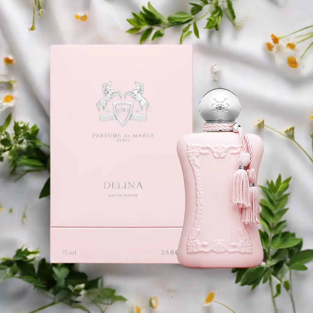 A professional product shot of the Parfums De Marly Delina perfume bottle and box. The image highlights the bottle's elegant, frosted pink glass, the decorative tassel, and the brand's iconic emblem.