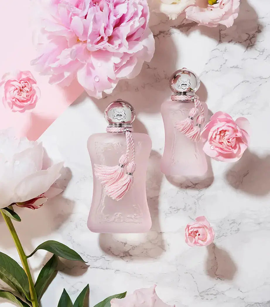 A dynamic product shot of the Parfums De Marly Delina bottles, set against a backdrop of beautiful pink floral arrangements, emphasizing the perfume's key notes.